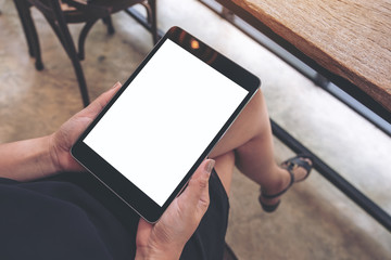 Top view mockup image of a woman sitting cross legged and holding black tablet pc with blank white desktop screen in cafe