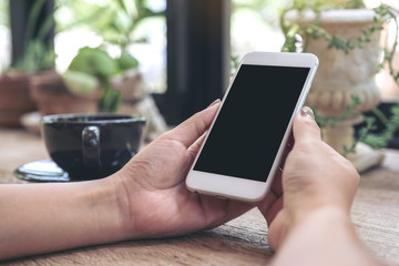 Mockup image of woman's hands holding white mobile phone with blank blank desktop screen and coffee cup on table in cafe