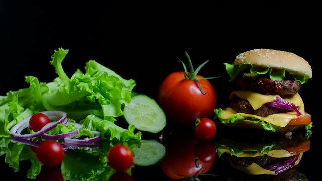 Fresh vegetables and tasty burger with cheese and beef cutlets on the black background