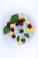 Red and yellow cherries on a white plate, fresh multicolored cherries with green leaves, yellow and red berries in the style of minimalism, vegetarian food, blank for the designer