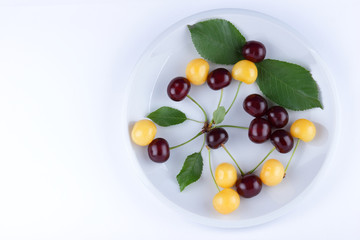Red and yellow cherries on a white plate, fresh multicolored cherries with green leaves, yellow and red berries in the style of minimalism, vegetarian food, blank for the designer
