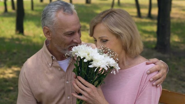 Pretty aged woman taking flowers from man, old couple date in city park, love