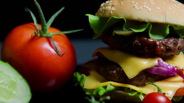 Close up of fresh vegetables and tasty burger with cheese and beef cutlets on the black background