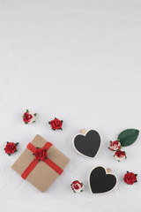 Brown gift box and tiny heart blackboard decorate with red rose paper flowers on white fabric with copy space