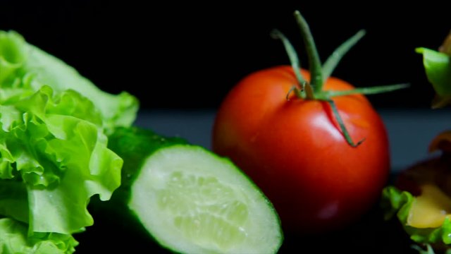 Close up of fresh vegetables and tasty burger with cheese and beef cutlets on the black background