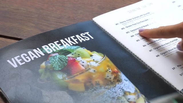 Closeup Of Female Hand Choosing Vegan Breakfast In Restaurant Menu