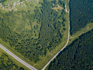 Top view of  road, a green forest and a large field in a warm sunny summer day. Helicopter drone shot.