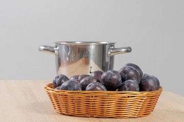 Basket full of ripe plums in front of a silver pot in the kitchen