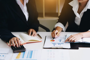 Business woman holding a pen pointing the graph and partnership to analyze the marketing plan with calculator on wooden table in office.
