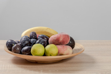 Different fruits like plums, lemons, peaches, or bananas in a flat basket 