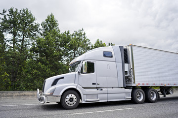 Big rig semi truck with reefer trailer and grille protection running on the white road