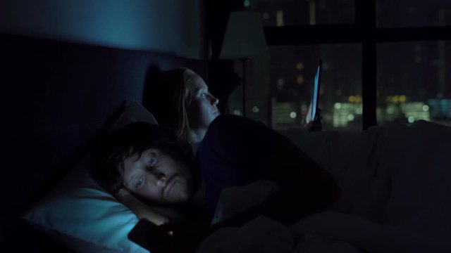 man and woman lying in bed each with smartphone and tablet pc. problems in marriage and intersexual relationship problems and mobile devices addiction concept