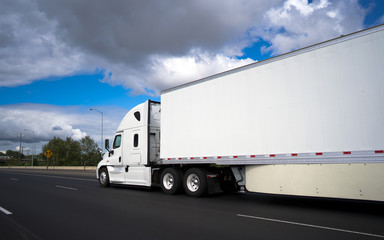 Long haul big rig semi truck transporting commercial cargo in dry van semi trailer on the wide highway with clouds sky © vit