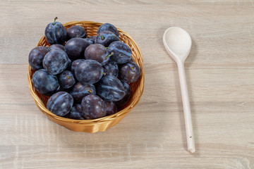 Wooden spoon beside a basket full of ripe plums