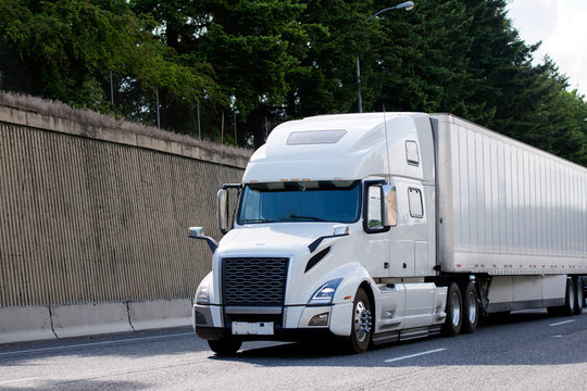 Elegant powerful big rig semi truck transporting dry van semi trailer on the road with side wall