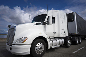 White big rig semi truck with black tented semi trailer transporting commercial cargo on the road