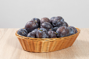 Front view of a basket full of ripe plums on a wooden table