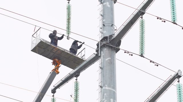 employees fix insulators on high voltage line from crane cradle