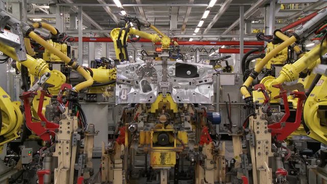 The group of robots in an automatic mode perform joint work on assembling and welding of the body of a modern car