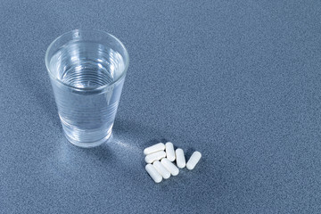 Top view of a glass full of water beside some white pills on a table 