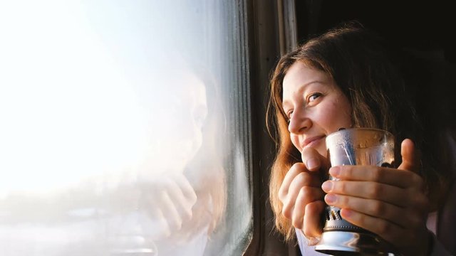 Beautiful Caucasian girl rides a train, drinks tea and looks out the window, 4k.