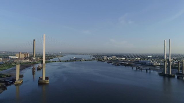 High level drone moves slowly towards Queen Elizabeth II Bridge as cargo ship departs Purfleet port	