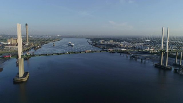 Drone rises slowly beside Queen Elizabeth II Bridge as cargo ship departs Purfleet port	