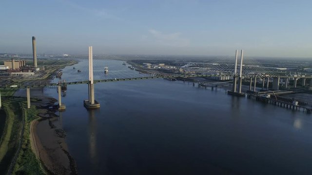 Drone flies slowly backwards from Queen Elizabeth II Bridge as cargo ship departs Purfleet port 
