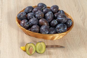 Basket full of ripe plums with a halved plum in front 