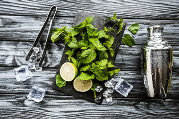 top view of ingredients for making mojito, tongs and shaker on wooden surface