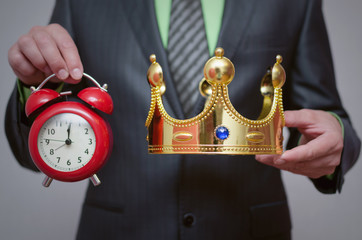 Businessman king holding in hands a gold crown and red alarm clock. Winner award ceremony time....