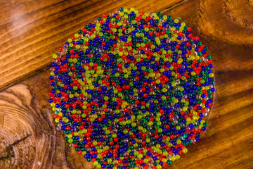 Multicolored hydrogel balls in a glass bowl on wooden table. Top view