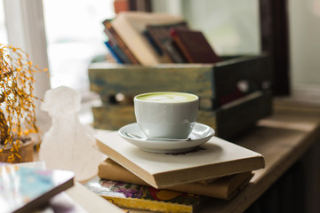Green tea matcha latte art in cup  cropped at an angle at a coffee shop cafe on wooden table with books near window. Background.