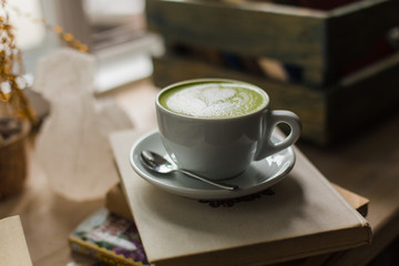 Green tea matcha latte art in cup  cropped at an angle at a coffee shop cafe on wooden table with books near window. Background.