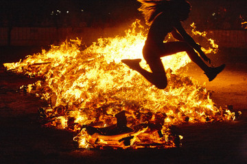Summer solstice celebration in Spain. Woman jump. Fire flames