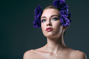 close-up portrait of beautiful young woman with eustoma flowers on head looking away isolated on grey
