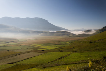Fototapeta na wymiar View of Castelluccio di Norcia (Umbria) at dawn, with mist, big meadows and totally empty blue sky