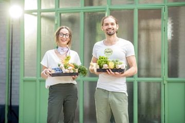 Portrait of a happy vegetarian couple holding boxe full of fresh raw vegetables outdoors on the green background