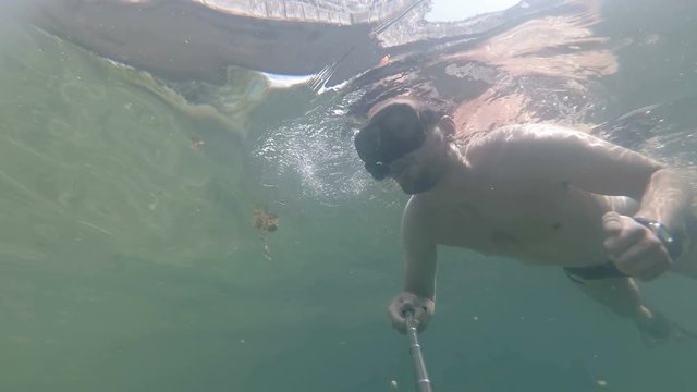 a man dives and makes a selfie under water.