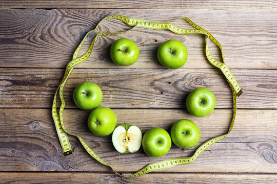 Smiling face of green apples and yellow centimeter tape on old wooden background. Apple dieting emoticon. Top view.