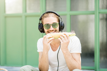 Funny musician playing harmonica with corn outdoors on the green background