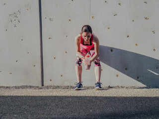  groggy sporty woman after fitness workout standing at a grey cement wall with shake bottle