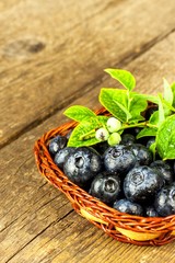 Wet blueberries in a small wicker basket. Freshly picked forest fruits on a wooden table. Sales of blueberries. Healthy summer refreshment.
