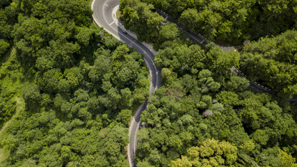 Aerial stock photo of car driving along the winding mountain pass road through the forest in Sochi, Russia. People traveling, road trip on curvy road through beautiful countryside scenery.