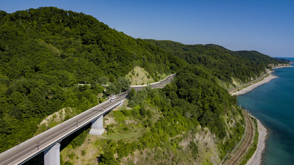 Fototapeta na wymiar Aerial stock photo of car driving along the winding mountain pass road through the forest in Krasnodar Krai, Russia. People traveling, road trip on curvy road through beautiful countryside scenery.