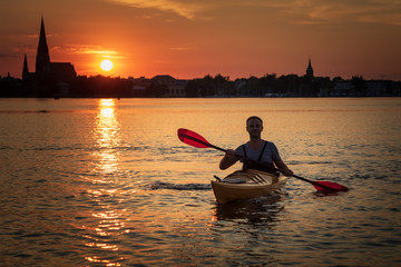 Mann in einem Kajak bei Sonnenuntergang vor der Skyline einer Stadt