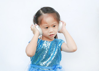 Adorable little Asian girl in bright dress listening music with headphones isolated on white background.