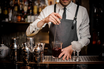 Barman stirring fresh summer alcoholic cocktail in glass