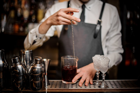 Barman stirring fresh alcoholic cocktail in glass