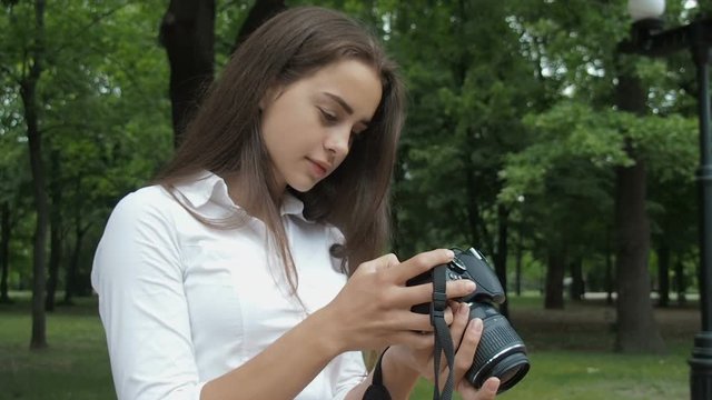 The girl looks through the photos on the camera. Beautiful teen girl with camera on nature.